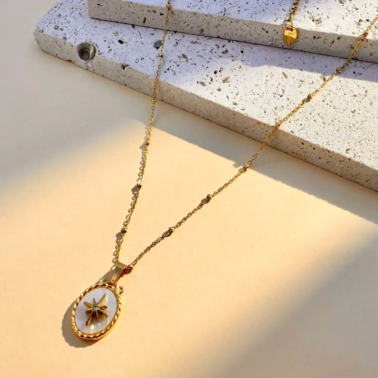 Collana in acciaio con pendente ovale in madreperla con stella e strass.